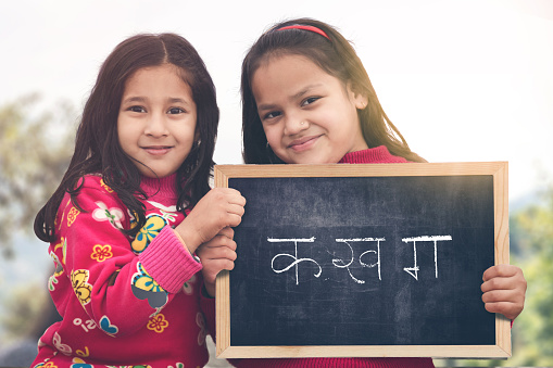 Adorable little 6-8 years old and 8-10 years old Indian/Asian girls smiling, holding hindi alphabet chalkboard.