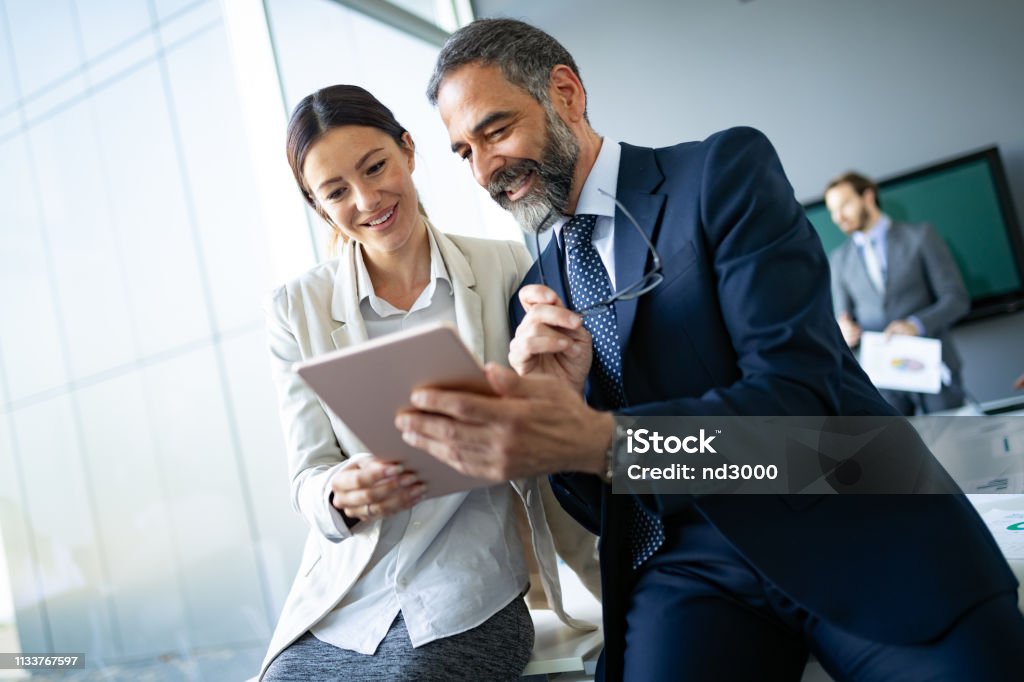Happy business colleagues in modern office using tablet Happy business colleagues in modern office talking and using tablet Business Stock Photo
