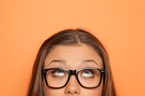 half portrait of a young girl with glasses looking up