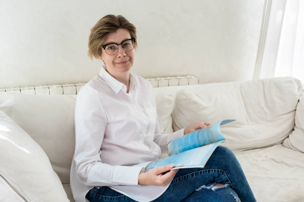 istock A middle aged woman sitting on a sofa reading a magazine. 1133782809