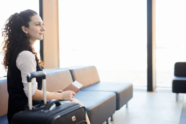 Side view portrait of young woman holding ticket and passport while waiting in airport, copy space
