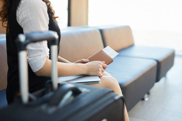 Side view of unrecognizable young woman holding ticket and passport while waiting in airport, copy space