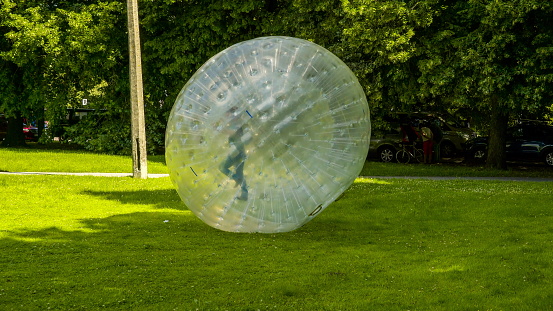 Kids playing the zorb ball on the grass pushing the zorb ball turn around and around