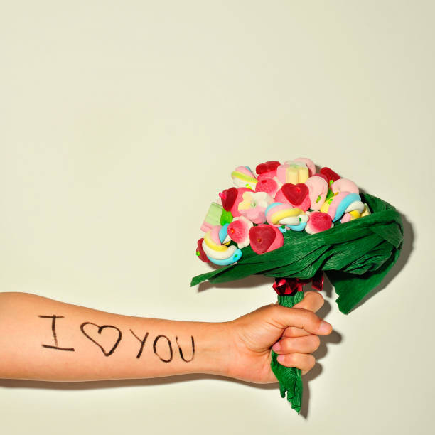 young man offering a candy bouquet a young man offering a candy bouquet and the sentence I love you written in his forearm forearm tattoos men stock pictures, royalty-free photos & images
