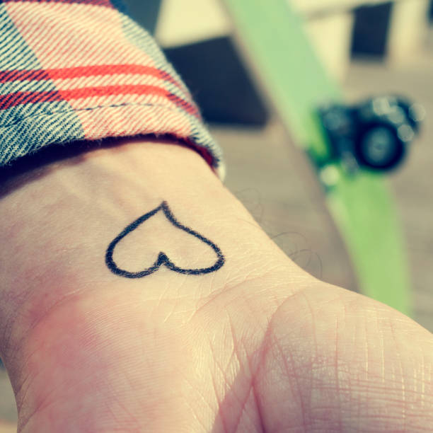 young man with a heart tattooed in his wrist closeup of the wrist of a young man with a heart tattooed in it arm tattoo ideas for men pictures stock pictures, royalty-free photos & images
