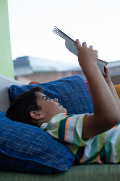 istock Schoolboy lying on sofa and reading a book in library 1133790031