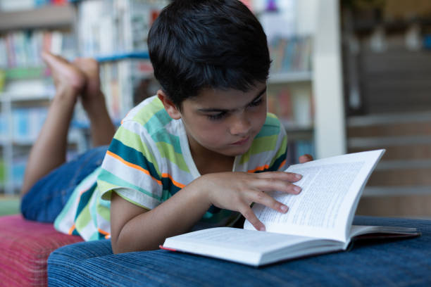 istock Schoolboy lying on sofa and reading a book in library 1133790084