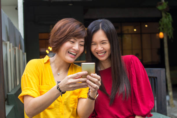 Fun in the coffee shop, two trendy females laughing over some jokes over the smart phone malaysianm LOL, women, friendship, happiness, laughing, asia, internet happy malay couple stock pictures, royalty-free photos & images