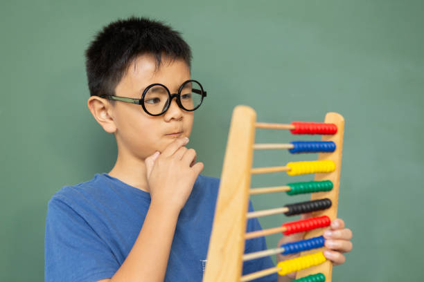 istock Thoughtful boy learning math with abacus against green chalkboard in a classroom 1133792547