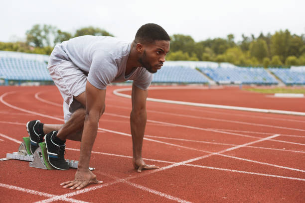 fit afro-amerikanischer läufer in startposition im stadion - männliche figur stock-fotos und bilder