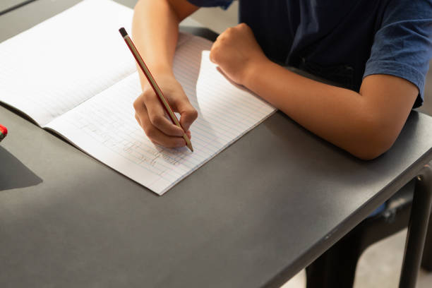 schoolboy skriver i en antecknings bok på skriv bordet i klass rummet - school bench above bildbanksfoton och bilder