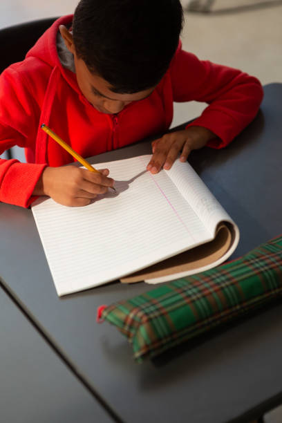 schoolboy skriver i en antecknings bok på skriv bordet i klass rummet - school bench above bildbanksfoton och bilder