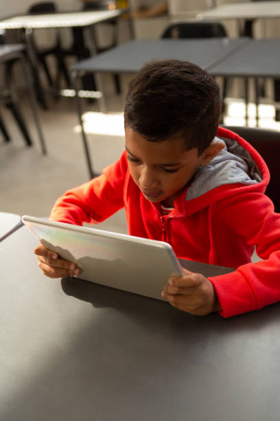 schoolboy använder digital tablett vid skriv bordet i ett klass rum - school bench above bildbanksfoton och bilder
