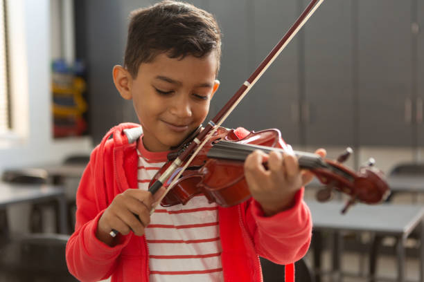 istock Smiling schoolboy with eyes closed playing violin in classroom 1133794165