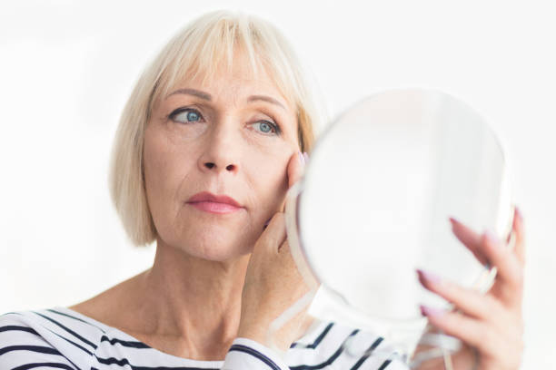 istock Elderly woman applying face cream, looking at mirror 1133797366