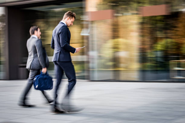 Blurred motion of businessmen using digital tablet and smart phone while walking outdoors.