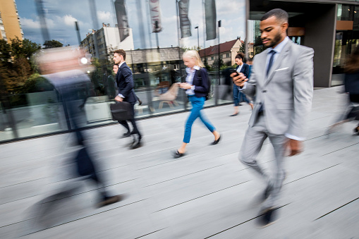 Blurred motion of businessmen and businesswomen using smart phone outdoors.