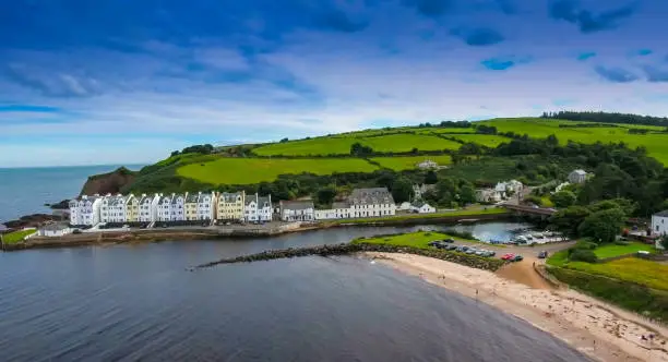 Aerial shot of the houses in the Cushendun Village near the coast of the big sea and the big mountain on the back