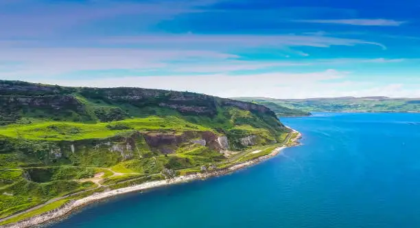 Amazing aerial shot of the blue sea and mountain in Cushendun the beautiful landscape view showing the greenish mountain with the small road fronting the blue sea