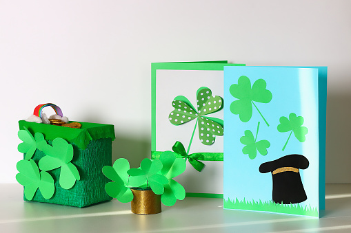 Diy St. Patricks Day greeting card made of cardboard and paper clovers on a gray background. Gift idea, decor Spring, Patrick Day. Step by step. Top view. Process kid children craft.