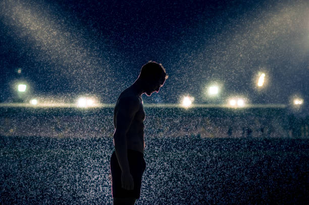 The Weight of Fame A shirtless Caucasian sporty male sideview silhouette looking down in the dark and rain with a stadium with lights backlit illuminating the raindrops Cape Town South Africa anti doping stock pictures, royalty-free photos & images