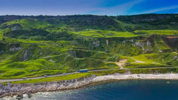 Aerial shot of the beautiful mountain in Cushendun Ireland there is a long road on the mountain side with a bus and cars travelling in Ireland