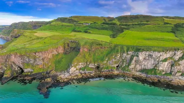 Aerial landscape view of the big island in Carrick-a-Rede in North Ireland where seen the green grasses on the cliff and the blue sea in Ireland