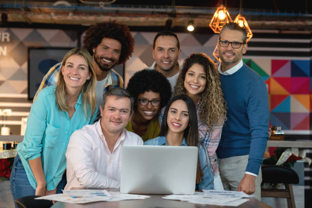 istock Diverse team of professionals at a coworking space all facing camera smiling while working with a laptop and documents 1133804306