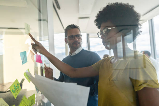 istock Team at the office brainstorming ideas looking very serious woman holding documents and pointing at adhesive notes on glass window 1133804318