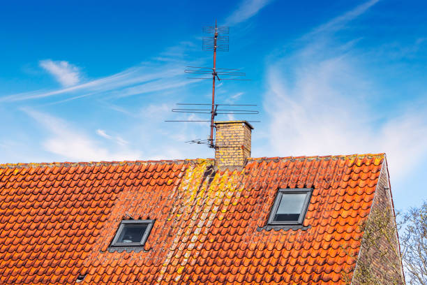 Rooftop with an antenna and a chimney under a blue sky in the summer with two small windows beneath