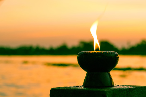 Candle light fire lamp nearby abstract background river during sunset or sunrise in countryside. Melting candlestick in evening twilight. Religion abstract concept.