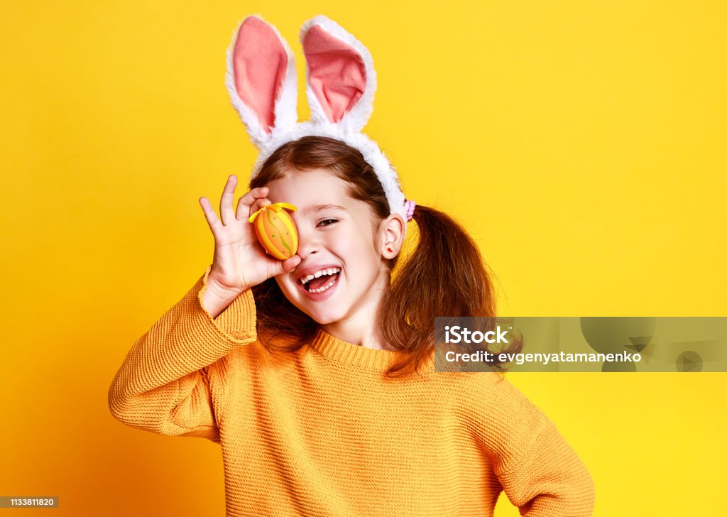 Lustige fröhliche Kindermädchen mit Ostereiern und Kaninchenohren auf gelb - Lizenzfrei Ostern Stock-Foto