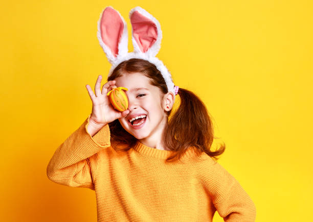 黄色のイースターエッグとバニー耳を持つおかしい幸せな子供の女の子 - easter egg easter yellow paint ストックフォトと画像