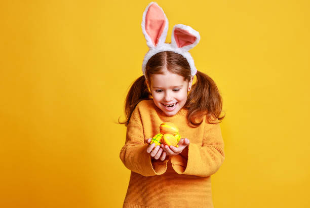 黄色のイースターエッグとバニー耳を持つおかしい幸せな子供の女の子 - easter egg easter yellow paint ストックフォトと画像