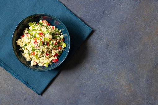 Tabbouleh salad with couscous, parsley, lemon, tomato, olive oil. Levantine vegetarian salad. Lebanese, arabic cuisine. Dark background. Top view. Space for text