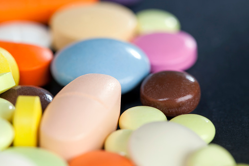 A large number of multi-colored tablets and pills lying together in a chaotic manner. scattered on the surface, closeup photo
