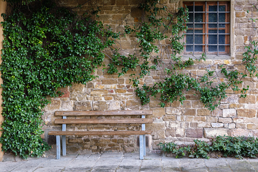 Wooden bench beside an ivy-clad sandstone wall and iron-barred window