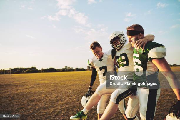 American Football Players Carrying An Injured Teammate Off The Field Stock Photo - Download Image Now