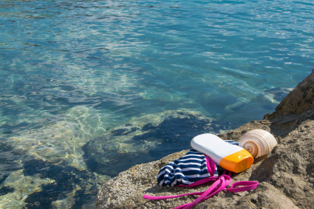 Beach items - swimwear, sun protection cream and a shell on a seashore rock