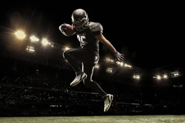 Photo of American football sportsman player on stadium running in action. Sport wallpaper with copyspace.