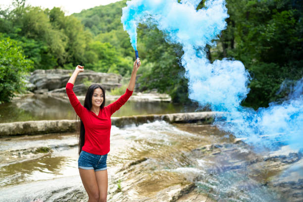 Young asian woman having fun in river, holding colored smoke stick.