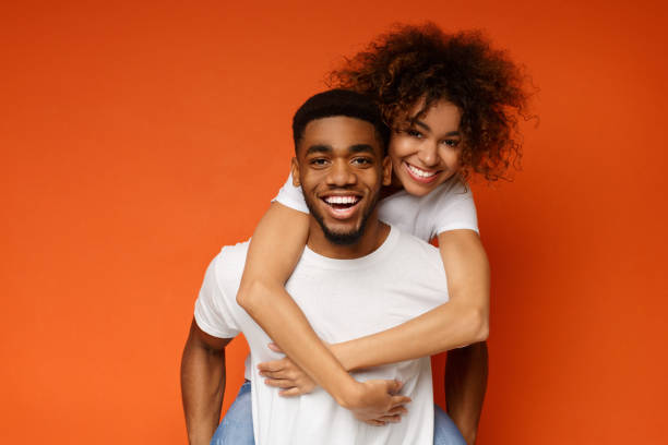 African-american couple having fun on orange background Man giving piggyback ride to his girlfriend. African-american couple having fun on orange background boyfriend stock pictures, royalty-free photos & images