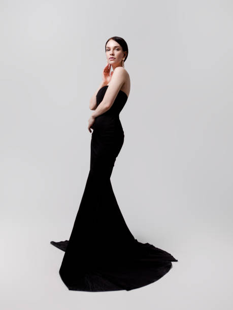 Beautiful young woman in luxury long black dress on gray background Full length portrait of young beautiful brunette woman wearing luxury strapless long black dress with train on white background. Designer clothing evening gown evening gown stock pictures, royalty-free photos & images