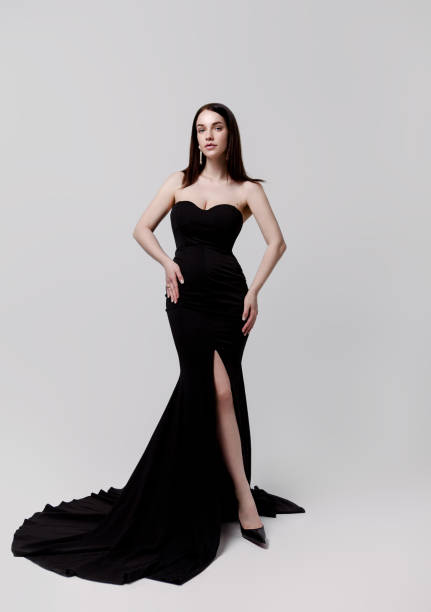 Beautiful young woman in luxury long black dress on gray background Full length portrait of young beautiful brunette woman wearing luxury strapless long black dress with train on white background. Designer clothing evening gown strapless stock pictures, royalty-free photos & images