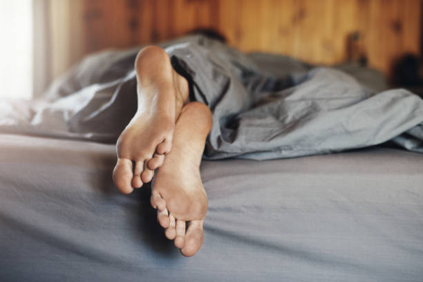 Closeup shot of a man's dirty feet while he's sleeping in bed