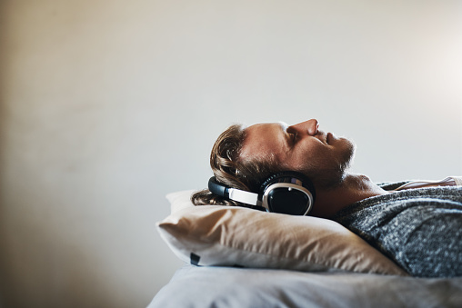 Shot of a handsome young man listening to music on his headphones while relaxing in bed at home