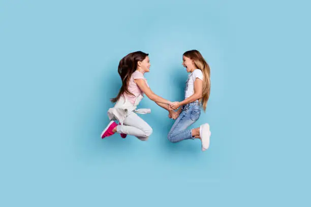 Photo of Full length body size profile side view of two people nice cute attractive cheerful straight-haired pre-teen girls having fun great weekend holding hands isolated over blue pastel background