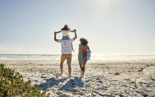 Summertime memories last a lifetime Rearview shot of a little girl and her parents spending time together at the beach lens flare offspring daughter human age stock pictures, royalty-free photos & images