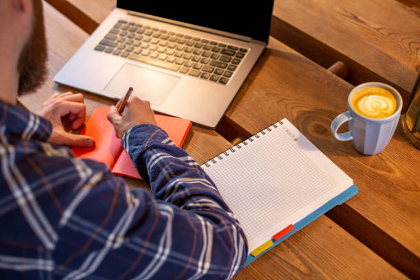 istock Cropped image of casual business man or freelancer planning his work on notebook, working on laptop computer with smart phone, cup of coffee on table at coffee shop or home office. 1133834334