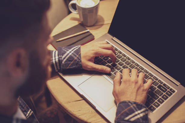 istock Young man drinking coffee in cafe and using laptop. Man's hands 1133834357